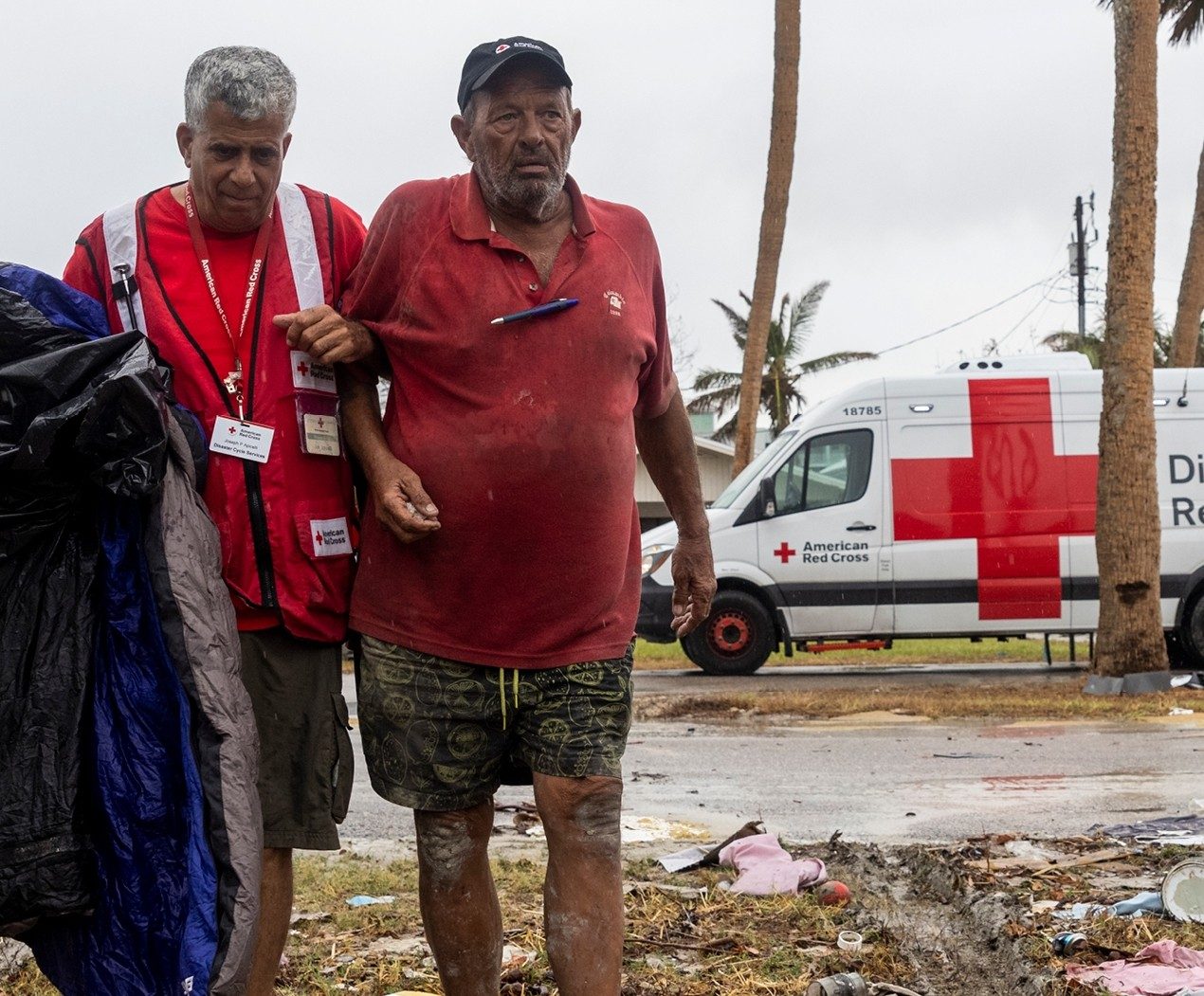 A Red Cross volunteer helps an injured older man walk