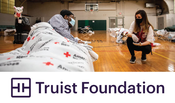Red Cross volunteer speaking with man inside shelter above Truist Foundation logo