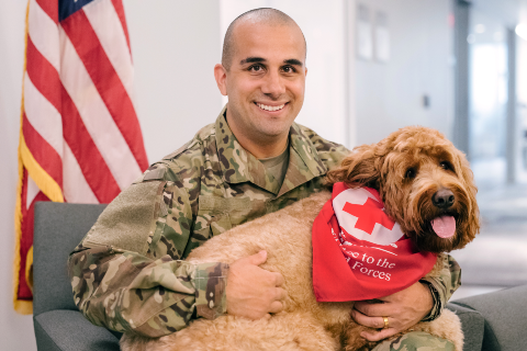 Military man holding dog wearing Red Cross bandana